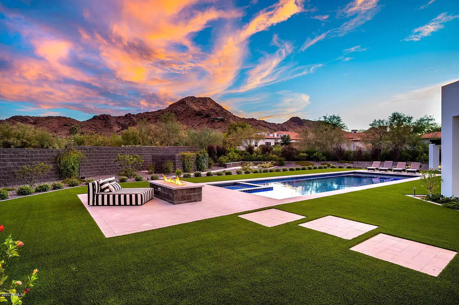 Backyard design featuring swimming pool, pavers, artificial turf, and mountain views under a sunset.